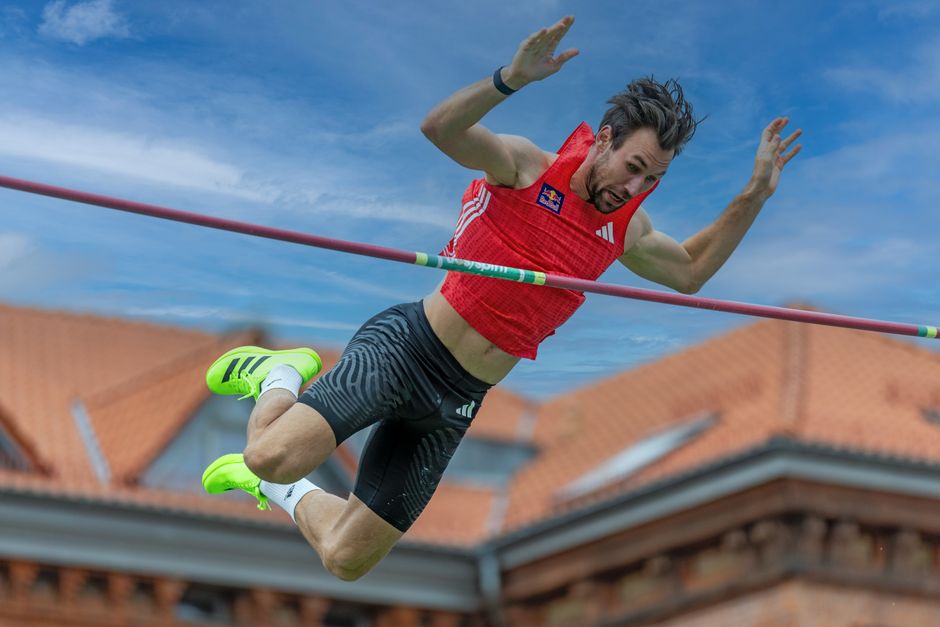 A male athlete captured mid-air during a pole vault attempt against a clear sky.