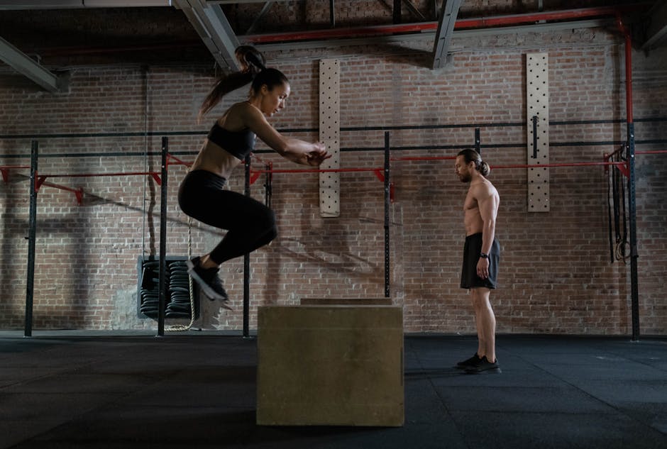 Female athlete performing box jump in gym watched by coach. Intense fitness training indoors.