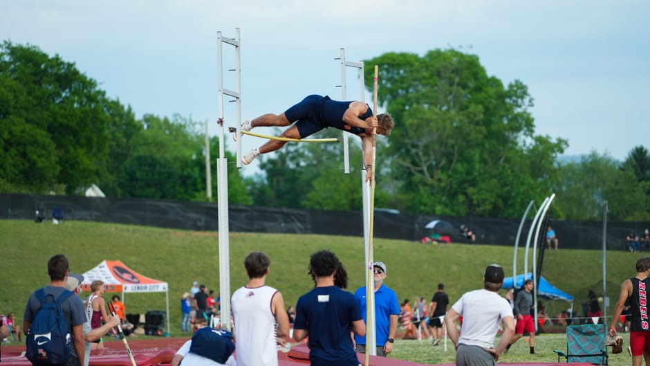 An athlete in action during a pole vault competition at an outdoor sports event with a crowd watching