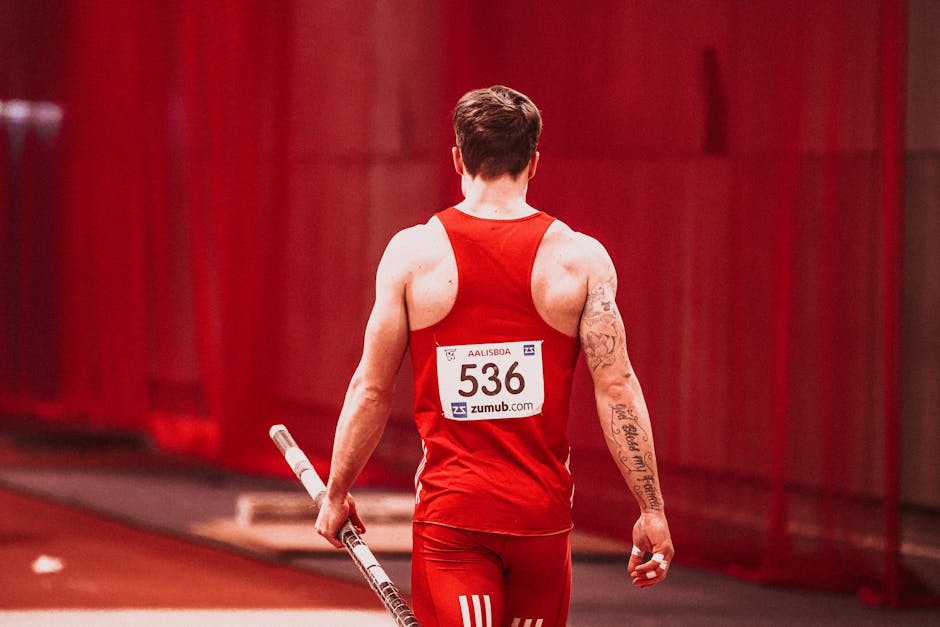 Rear view of male athlete holding pole, ready for vault in red sportswear