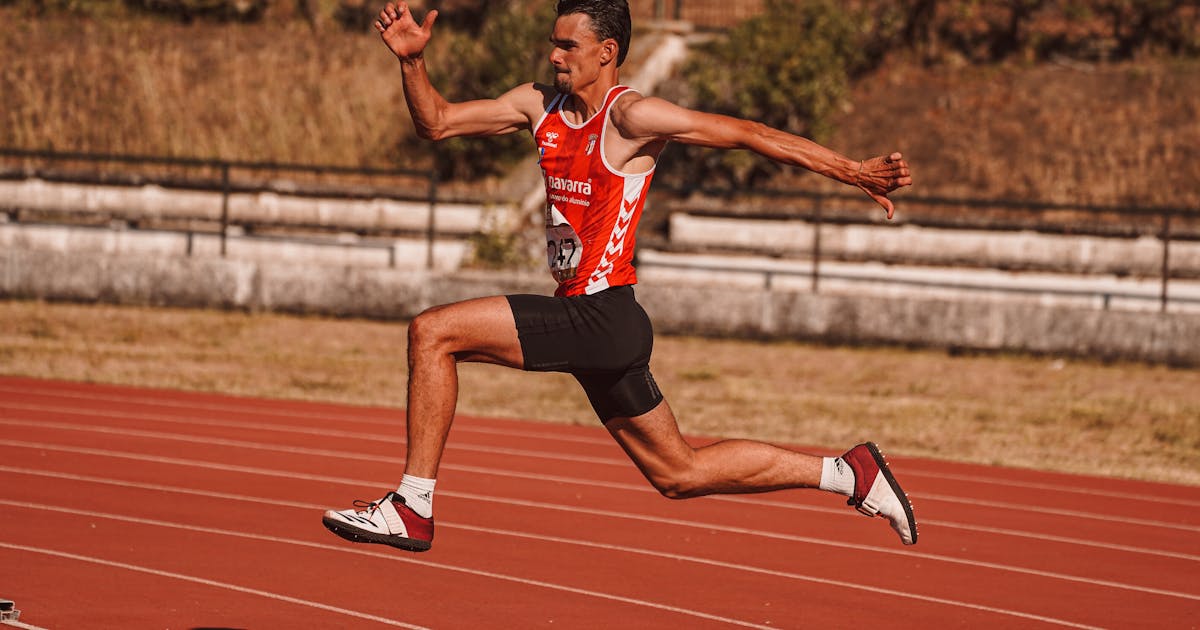 Athlete in mid-jump at a track event, demonstrating athletic technique