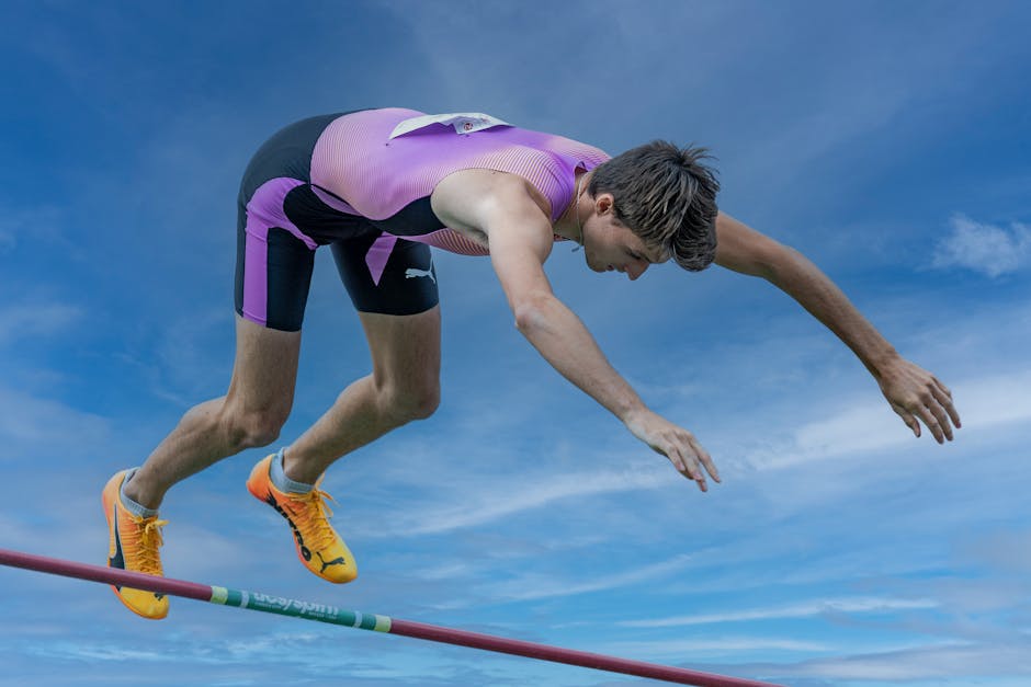 Male athlete performing a pole vault against a blue sky, demonstrating athleticism and focus