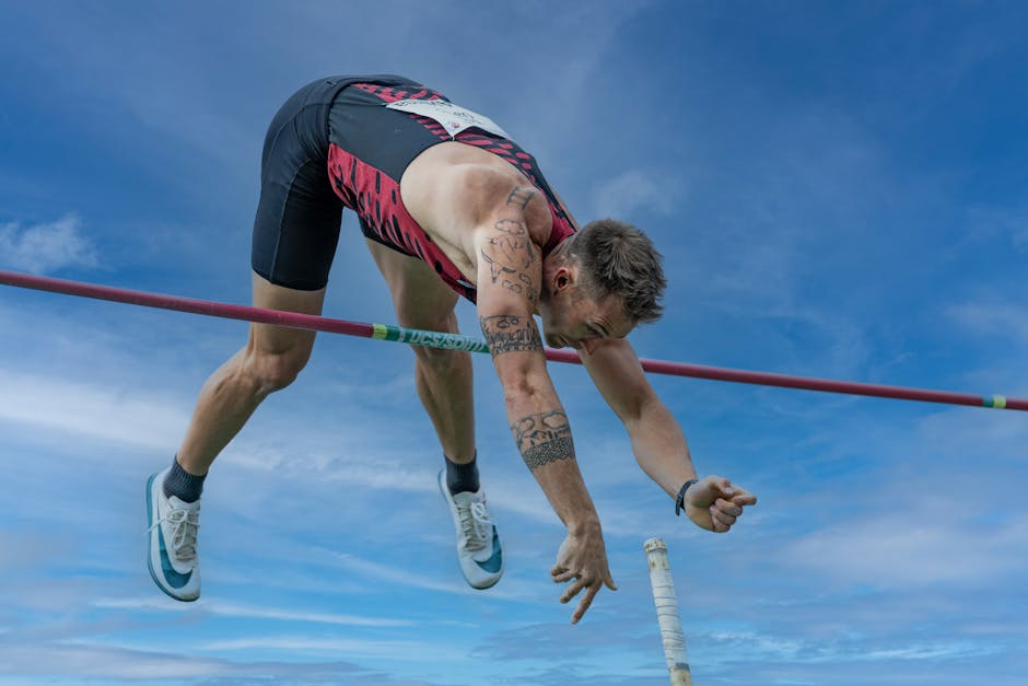 Dynamic shot of a pole vaulter in mid-air against a blue sky, showcasing athletic skill