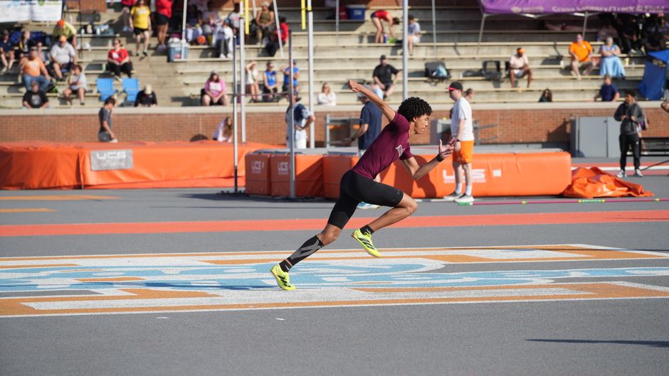 Athlete sprinting on track during a sunny outdoor sports meet.
