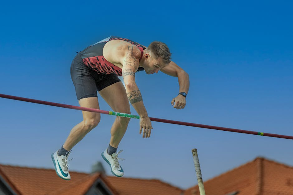 A determined athlete executes a pole vault under a clear blue sky, showcasing strength and focus.