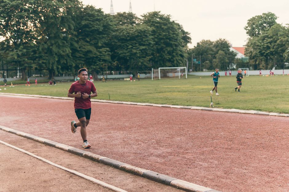 Athletes running and training on an outdoor track in a lush park setting.