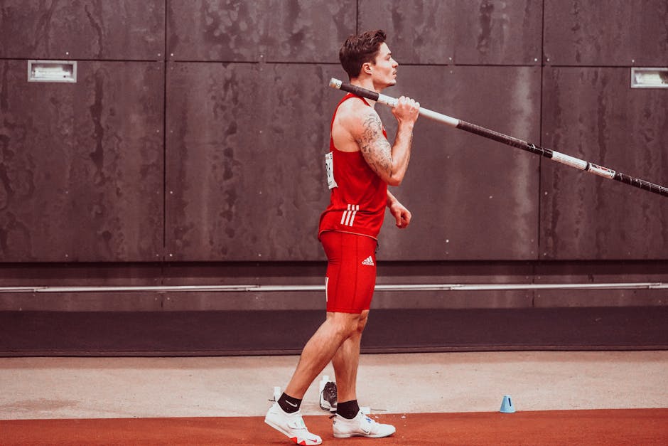 Athletic male in sportswear holding pole for pole vault indoors, showing determination and focus