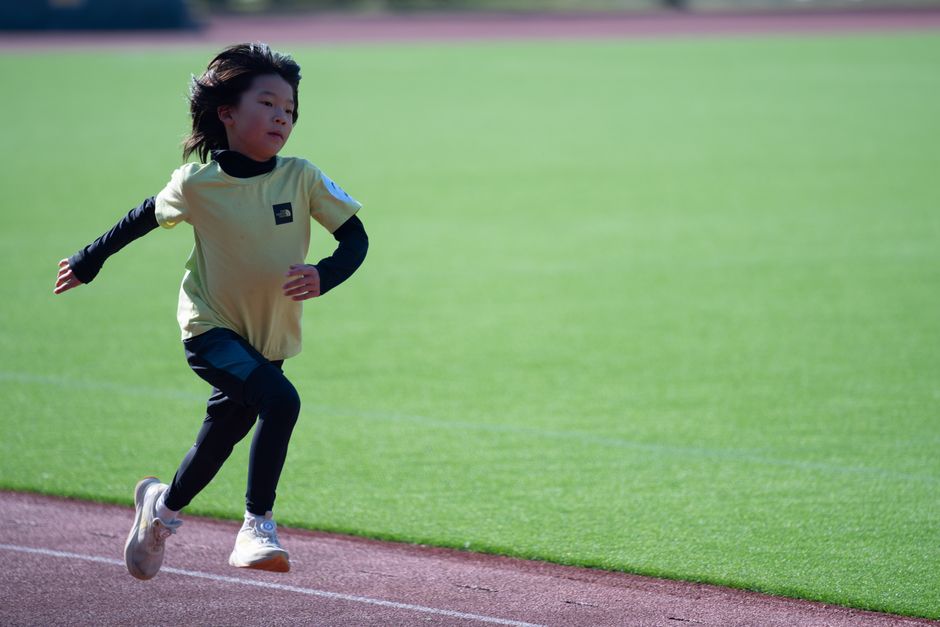 A young child running energetically on a track under sunny conditions.